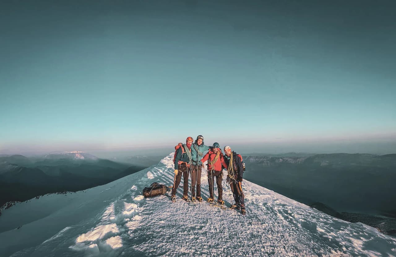 Four climbers pose on the snow-covered crest of Mont Blanc, with a breathtaking panorama.