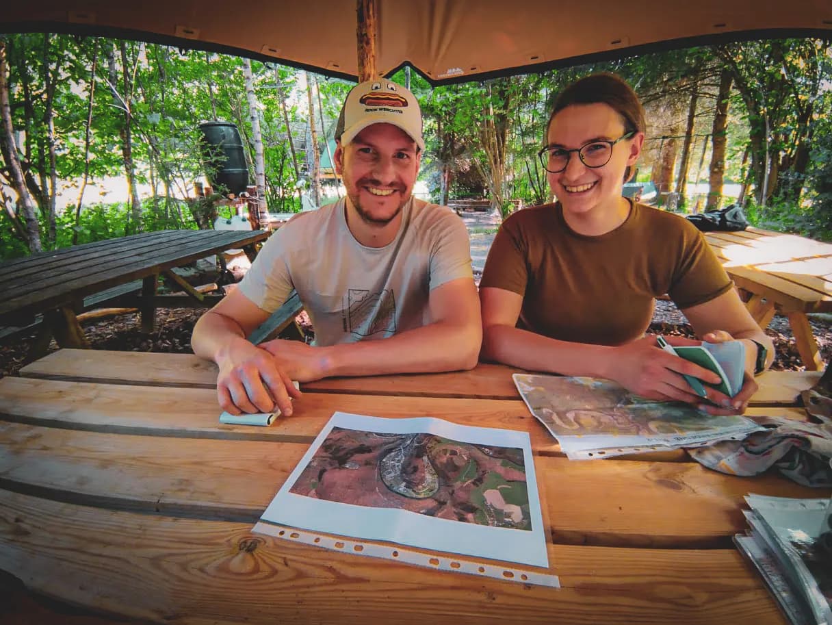 Twee lachende mensen rond een houten tafel, klaar voor een avontuur in het bos.