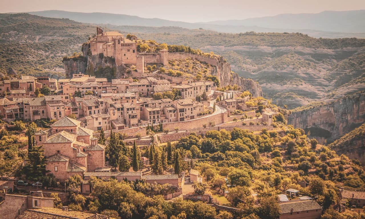 A picturesque village perched on a hill, surrounded by green, mountainous landscapes.