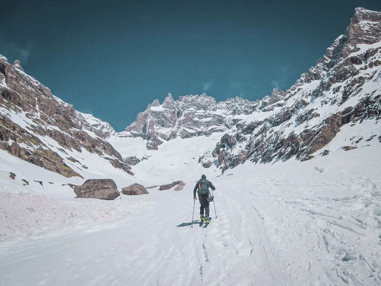 Un skieur solitaire avançant dans un paysage montagnard enneigé, sous un ciel bleu éclatant.