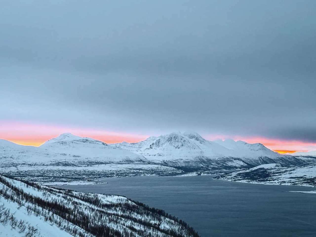 Een majestueus besneeuwd landschap, met bergen die worden verlicht door een pastelkleurige zonsondergang aan de oever van een fjord.