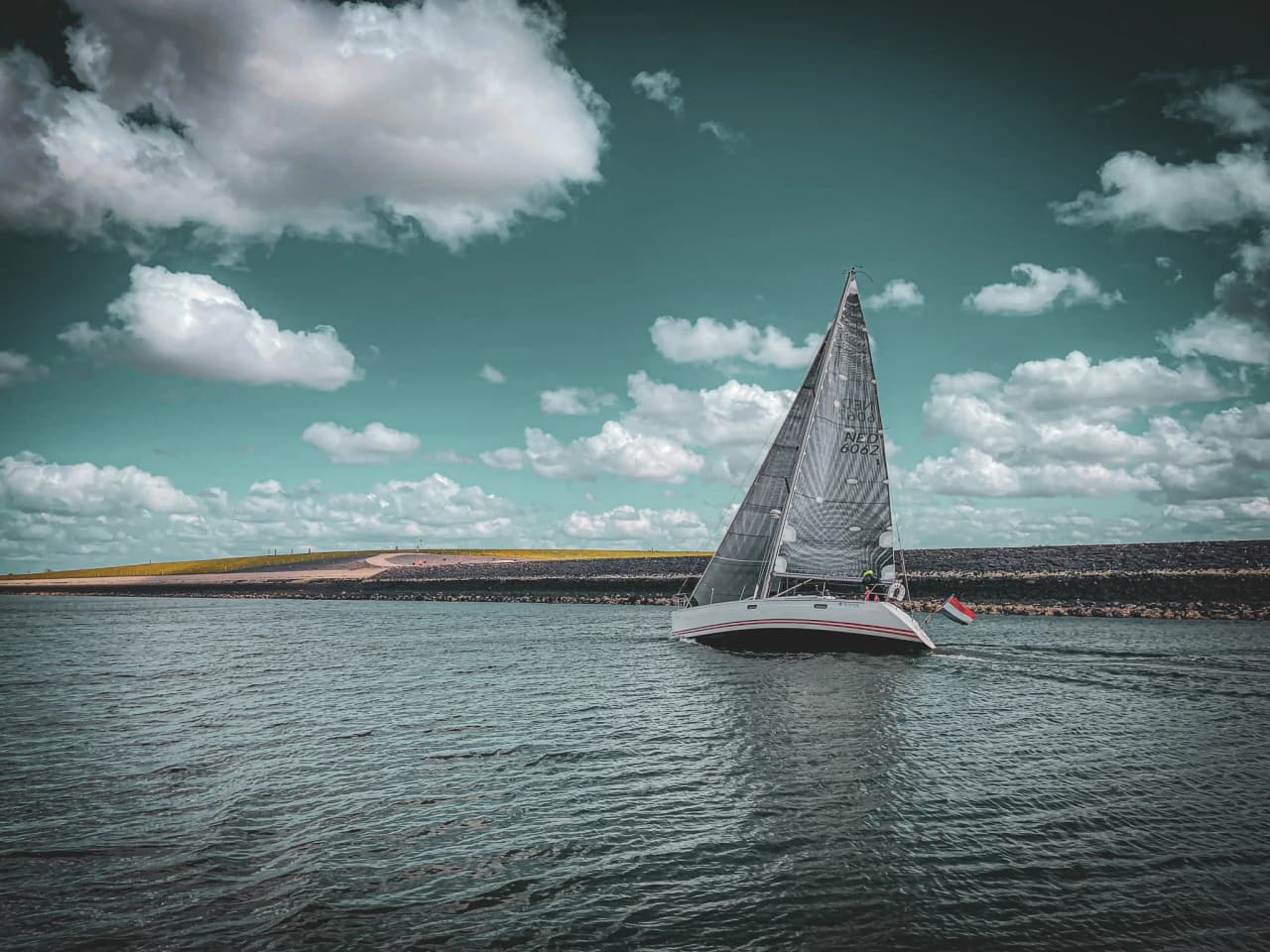 Zeilboot varend op rustig water onder een bewolkte hemel in Zeeland.