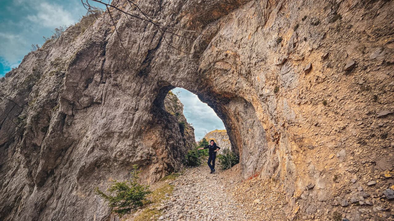 Twee wandelaars lopen hand in hand over een groen pad, omringd door majestueuze bergen.