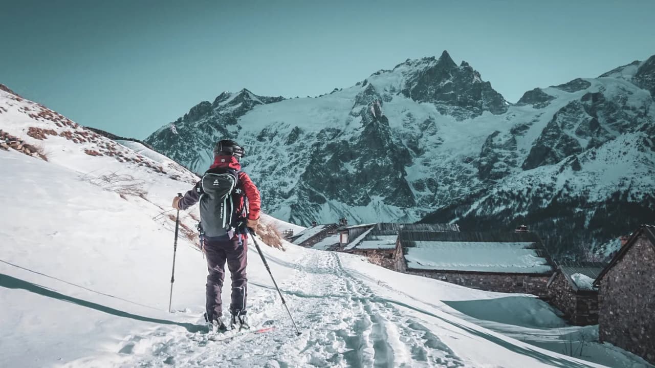Un skieur solitaire aventureux sur un sentier enneigé devant des montagnes majestueuses.