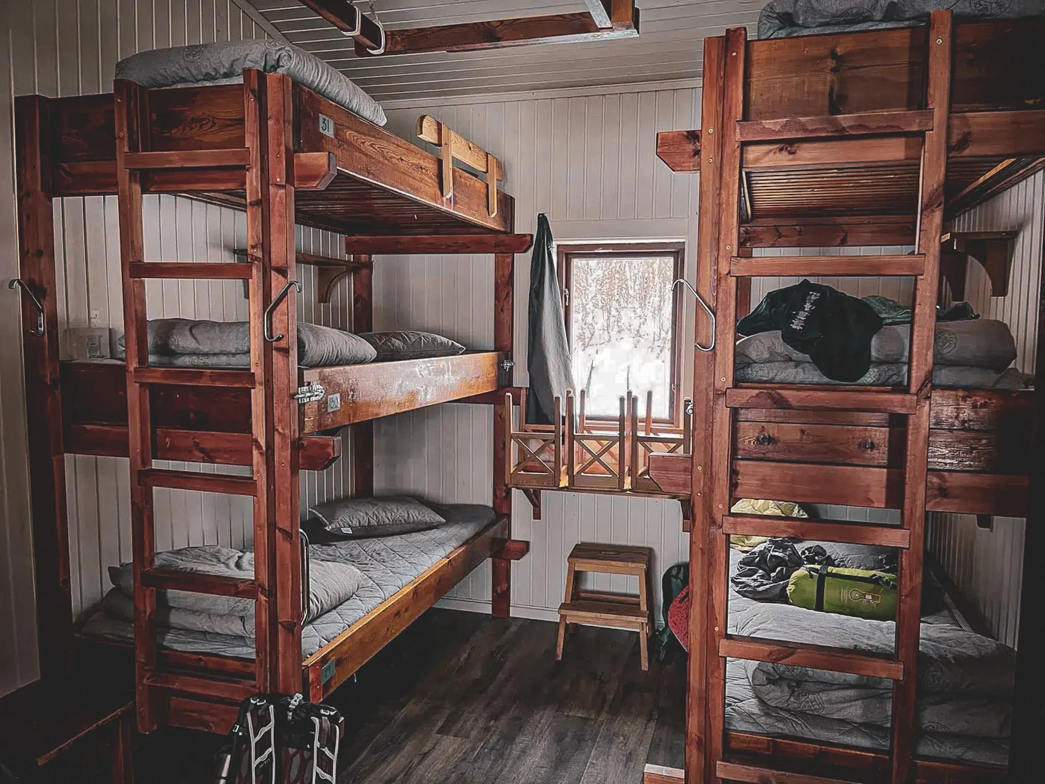 A room in an STF refuge with wooden bunk beds on either side of the room. The beds are covered with grey mattresses and cushions. There is a small wooden bench in the centre.