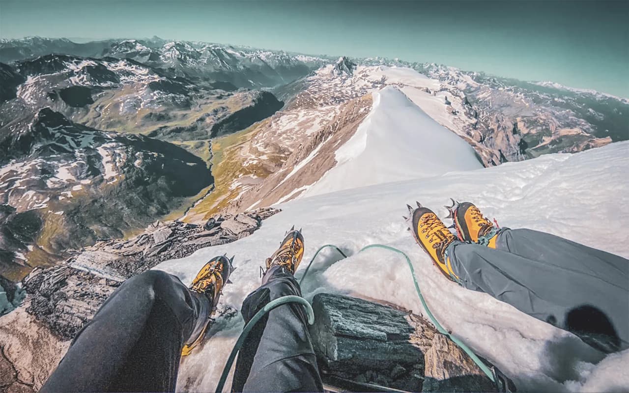 Deux alpinistes assis sur un sommet enneigé, admirant un panorama de montagnes majestueuses.