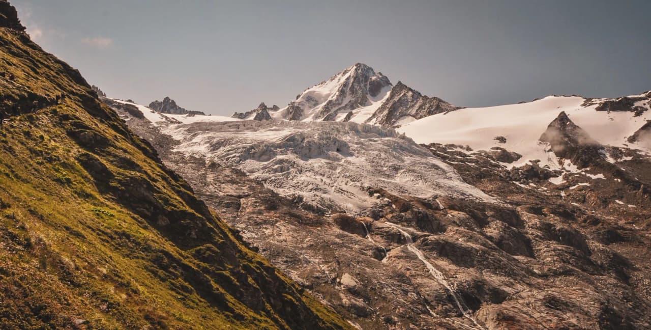 Een uitgestrekt Alpenpanorama van besneeuwde toppen en weelderig groene hellingen, een uitnodiging om te reizen.