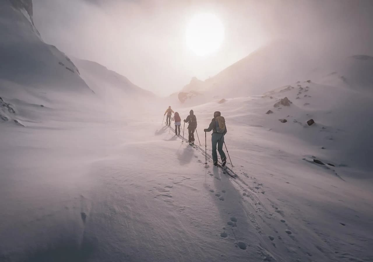 Groupe de randonneurs sur la neige, escaladant les Alpes italiennes sous un ciel brumeux.