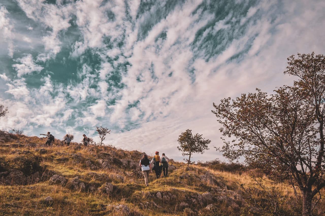 Een groep wandelaars op een gouden heuvel, onder een bewolkte hemel, midden op het Italiaanse platteland.