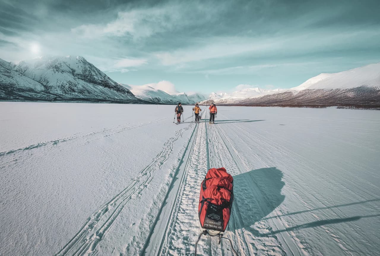 An expedition group snowshoes their way across a frozen lake surrounded by snow-capped mountains.