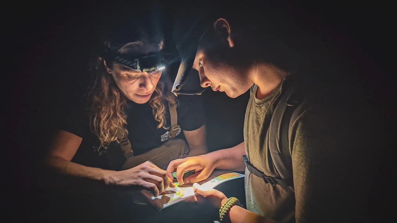 Deux personnes examinent attentivement une carte sous une lumière tamisée, en pleine nature.