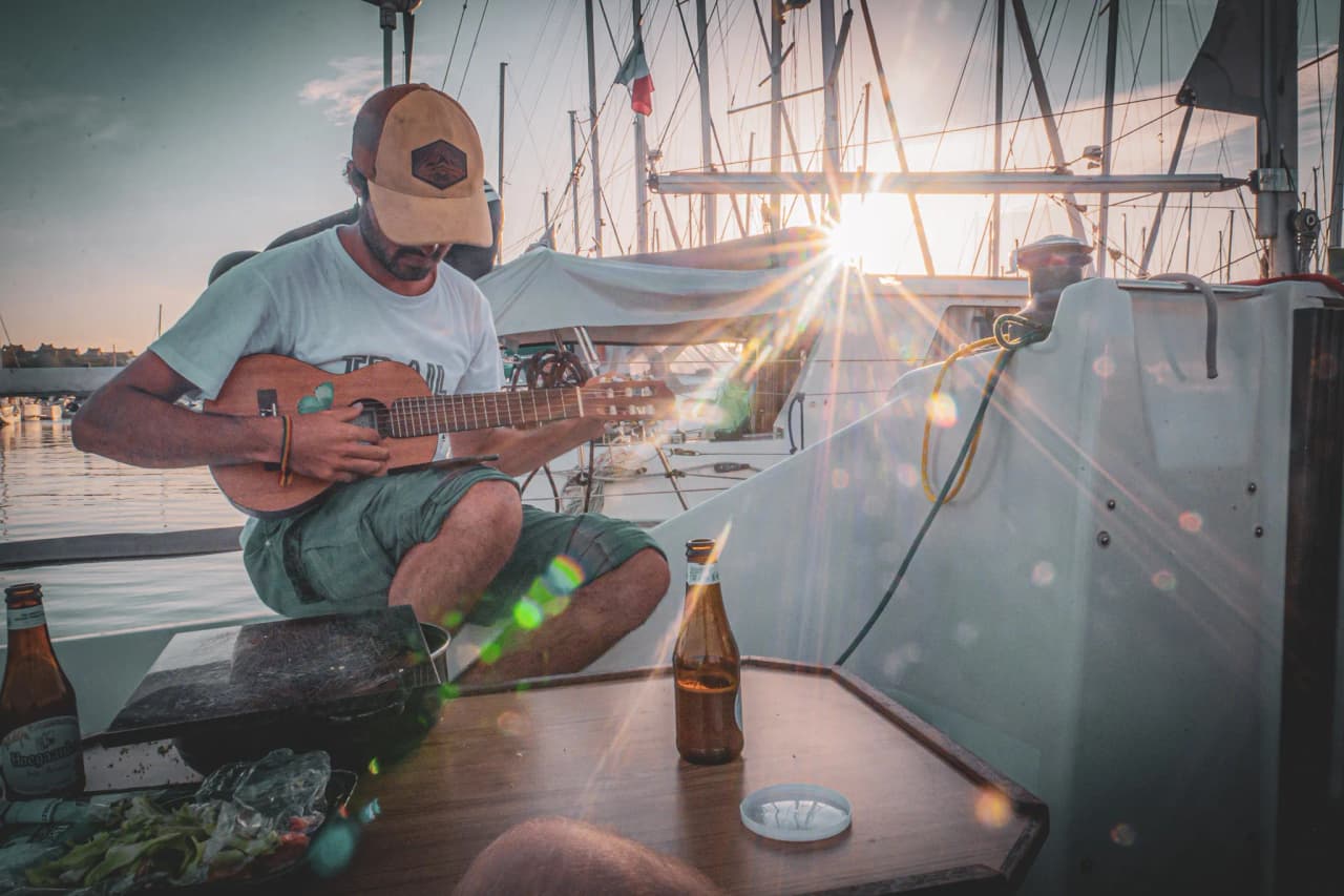 Muzikant op een zeilboot bij zonsondergang, ontspannen met een biertje en zeegezichten.