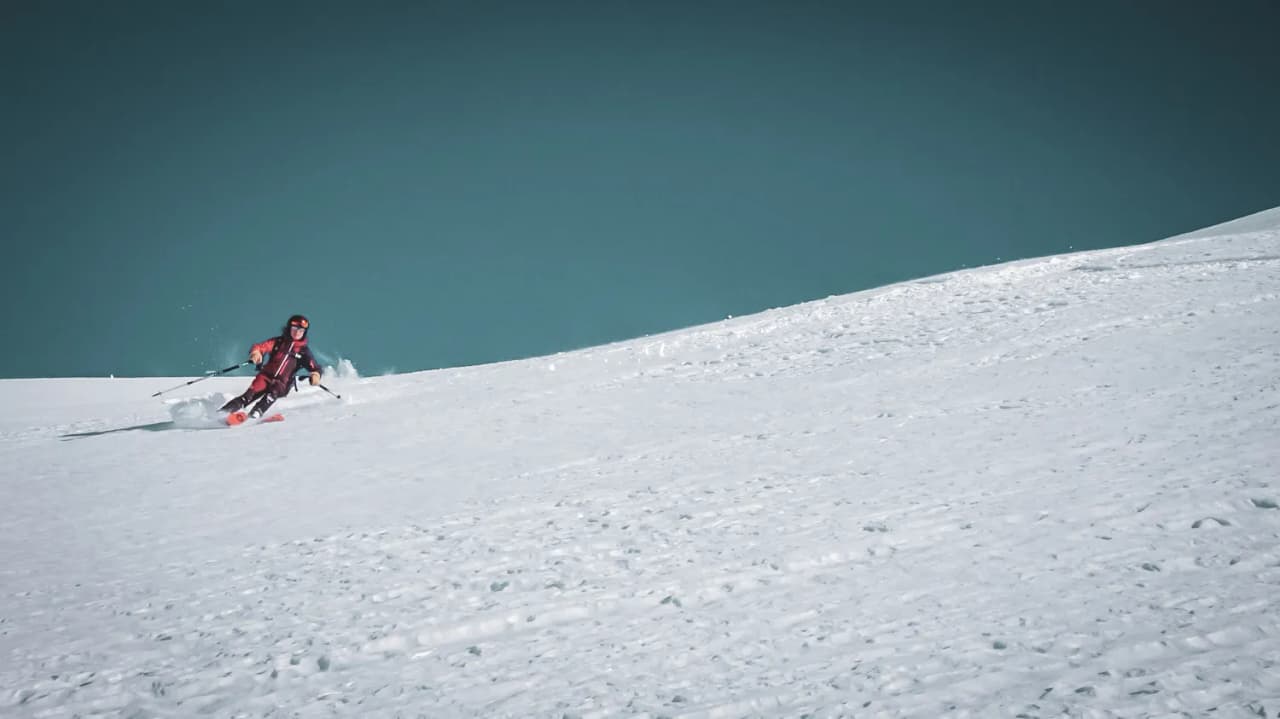 Ski de randonnée sur une pente vierge, paysage enneigé sous un ciel bleu éclatant.