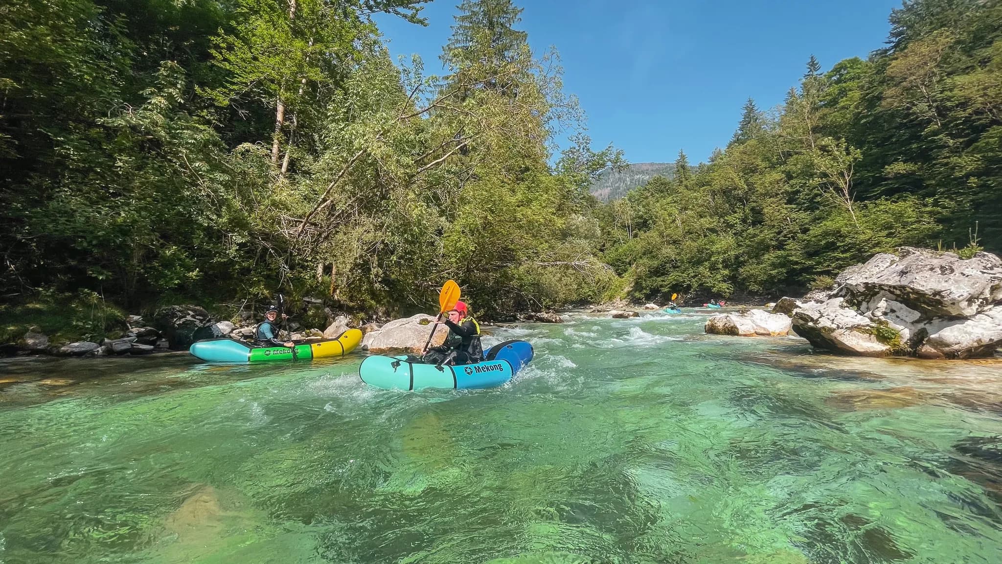 Deux packrafts glissent sur une rivière cristalline entourée de verdure luxuriante en Slovénie.