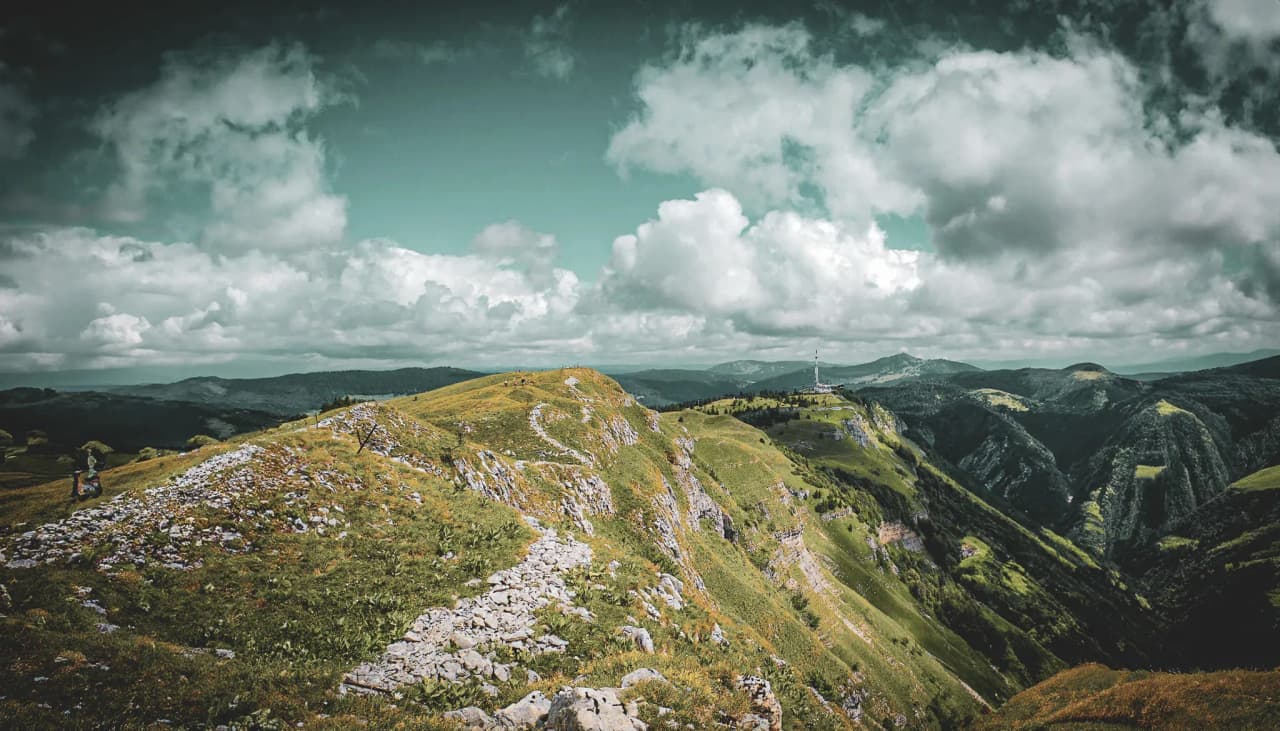 A panorama of the green crests of the Jura under a cloudy sky, an invitation to adventure.