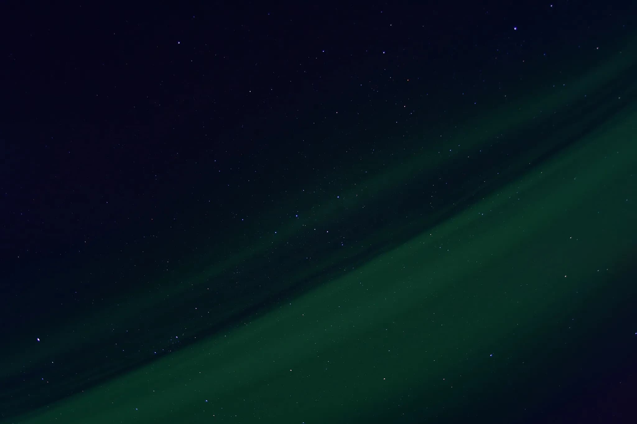 A night sky dotted with twinkling stars, where a faint green halo spreads out horizontally, creating a contrast with the dark hues of space. This scene evokes an atmosphere