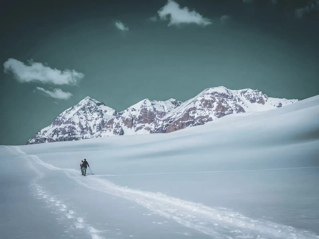 An adventurer on snowshoes on a vast snow-covered landscape, surrounded by majestic mountains.