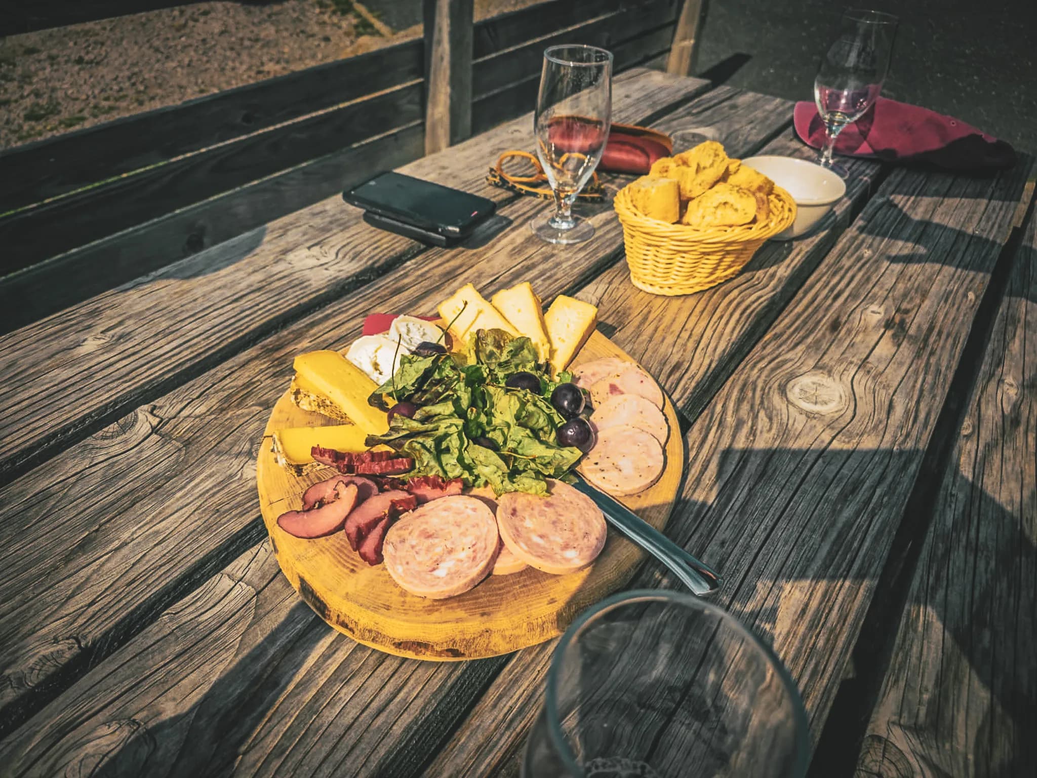 A wooden board displays an assortment of charcuterie and cheeses, including slices of ham, sausage and several types of cheese, accompanied by lettuce leaves and olives. Next to it,