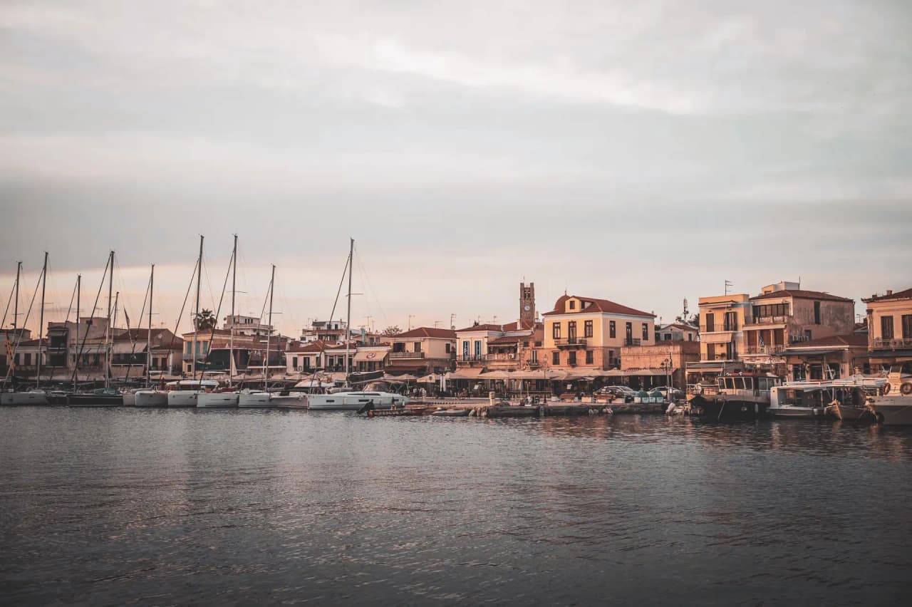 Un port pittoresque en Grèce avec des voiliers, des maisons colorées et une atmosphère méditerranéenne.