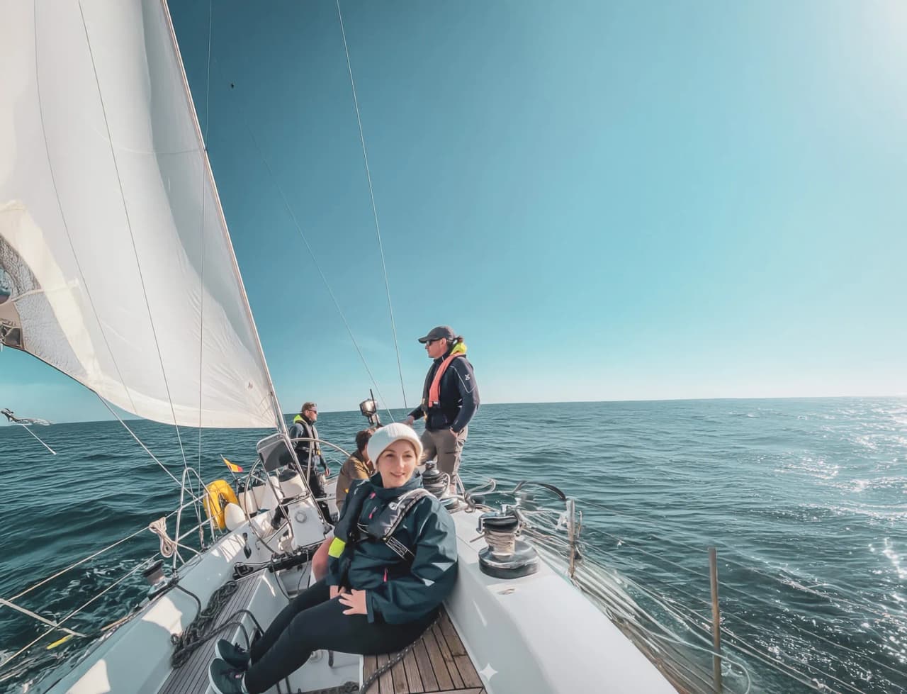 Un groupe navigue paisiblement en voilier au large, sous un ciel ensoleillé et des eaux turquoise.