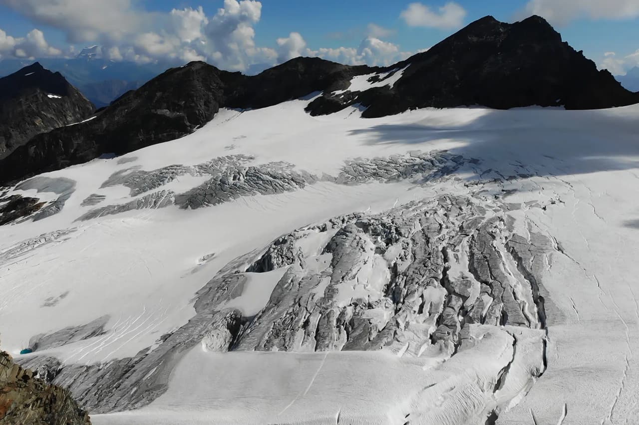 Vue panoramique d'un glacier majestueux, flanqué de montagnes sous un ciel ensoleillé. Une invitation à l'aventure alpine !