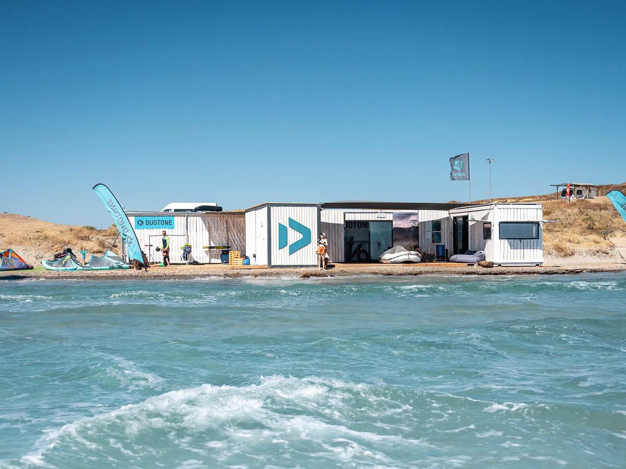 Un centre de kitesurf moderne sur une plage ensoleillée, entouré d'eaux turquoise.