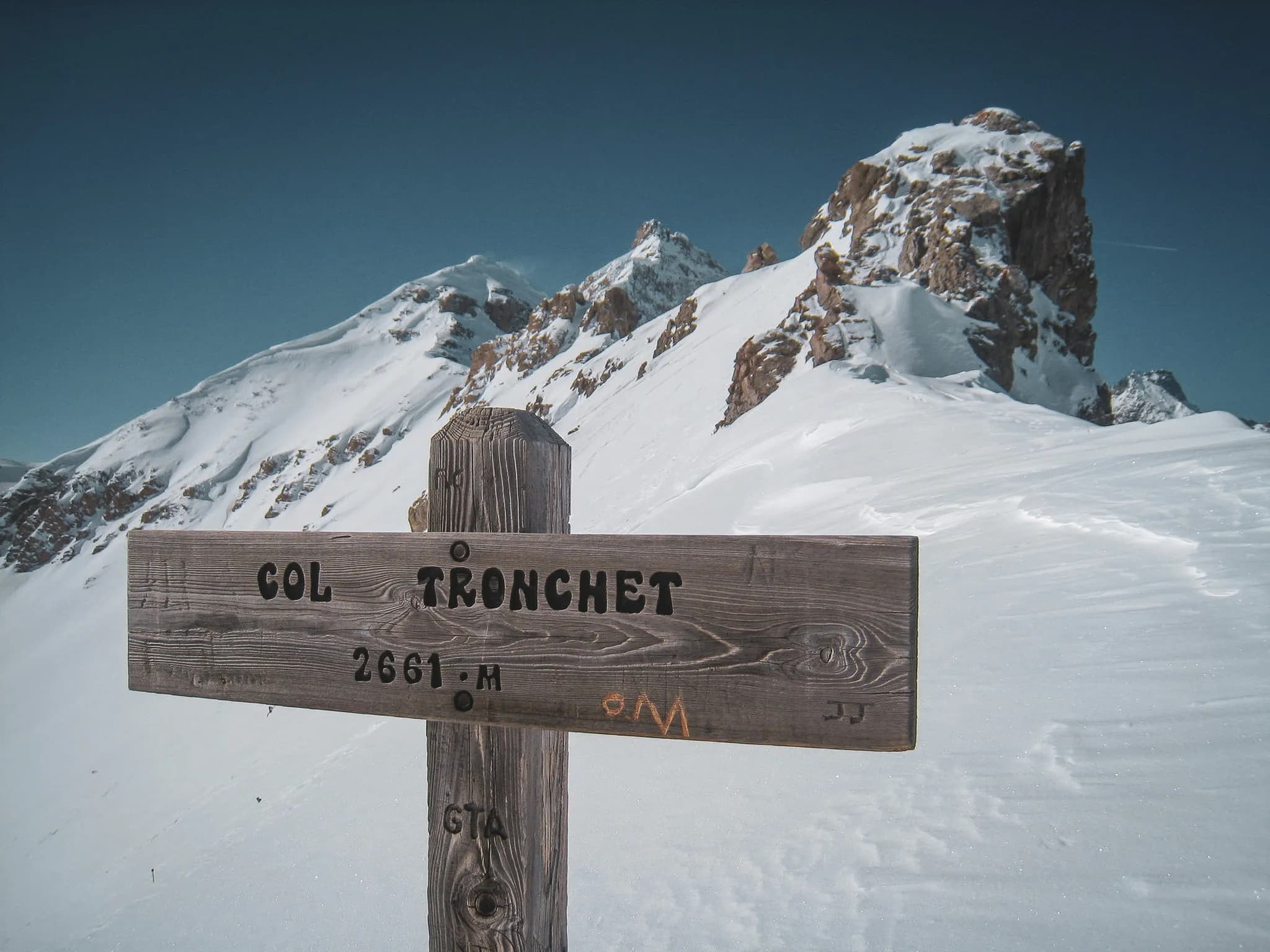 Wooden panel indicating the Col Tronchet, surrounded by majestic snow-capped mountains.
