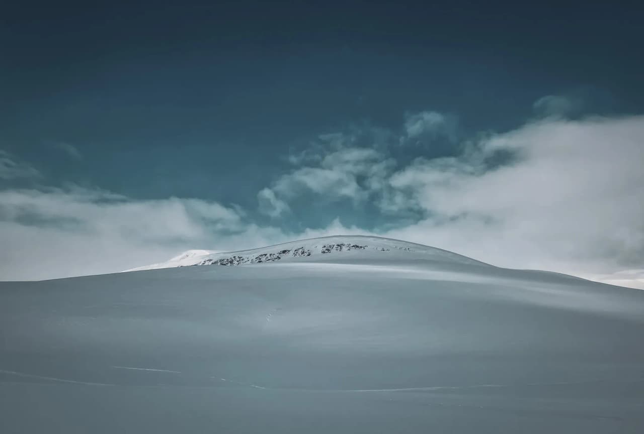 Een uitgestrekt besneeuwd landschap onder een blauwe hemel, een uitnodiging voor avontuur in Zweeds Lapland.