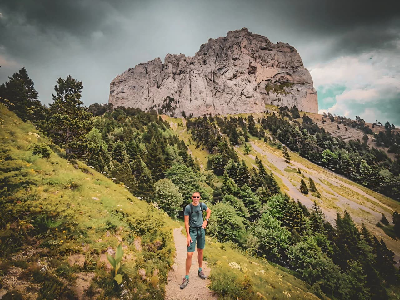 Smiling hikers with Mont Aiguille as a backdrop, in the heart of lush green countryside.