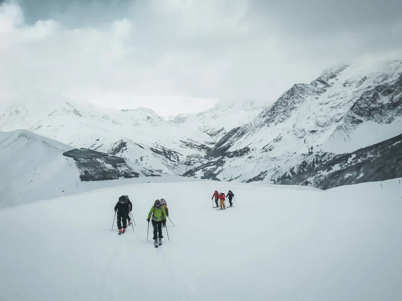 Groupe de skieurs de randonnée évoluant sur des pentes enneigées à La Grave, sous un ciel dramatique.