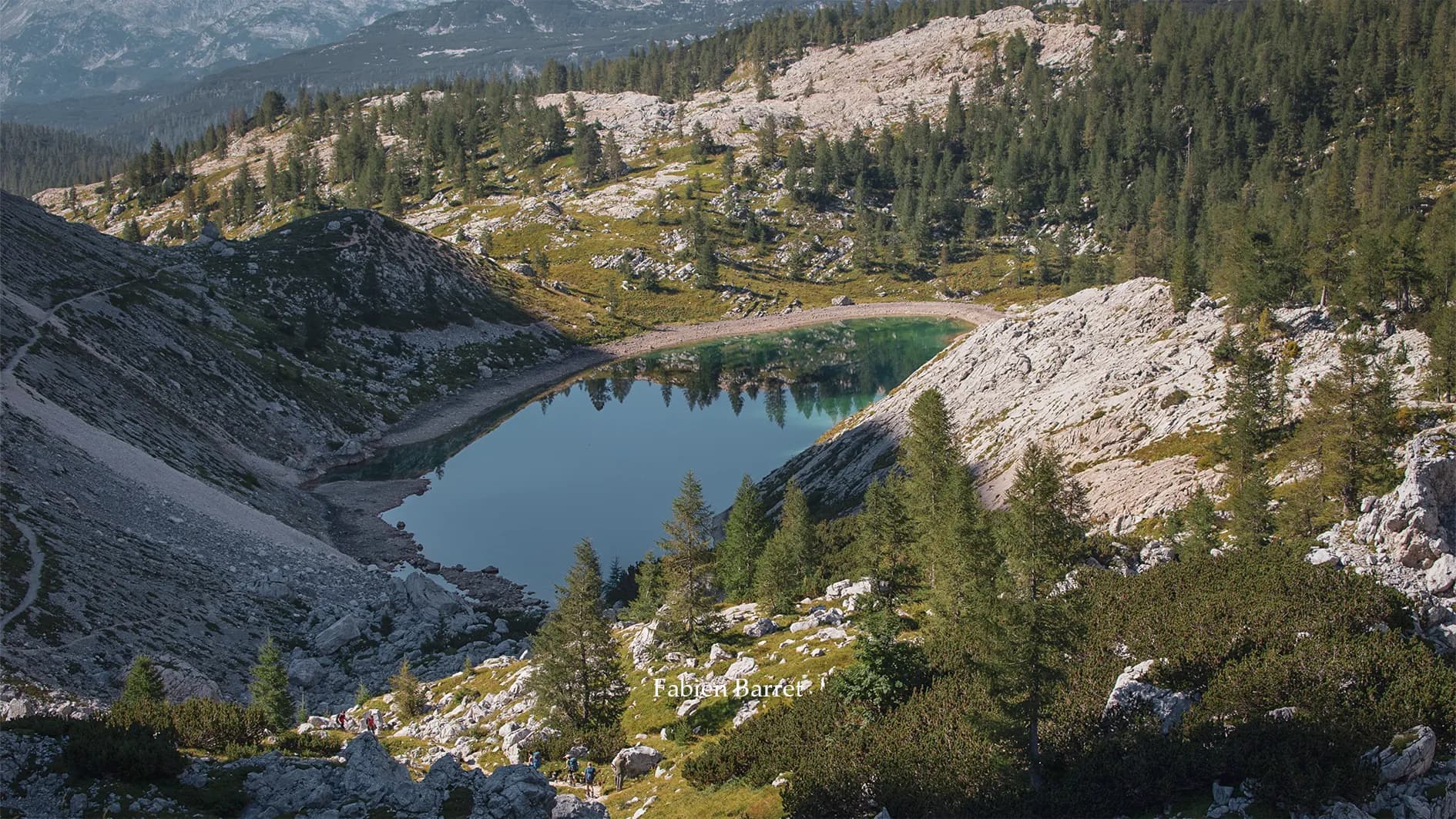 A group of hikers are making their way over rocky mountain terrain. They are carrying rucksacks and using walking sticks to help them on their ascent. The scene is surrounded by rock formations, with