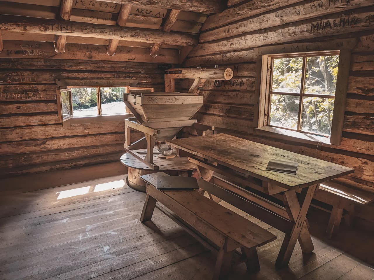 The rustic interior of a light-filled wooden chalet, with table and benches, is an invitation to get together.