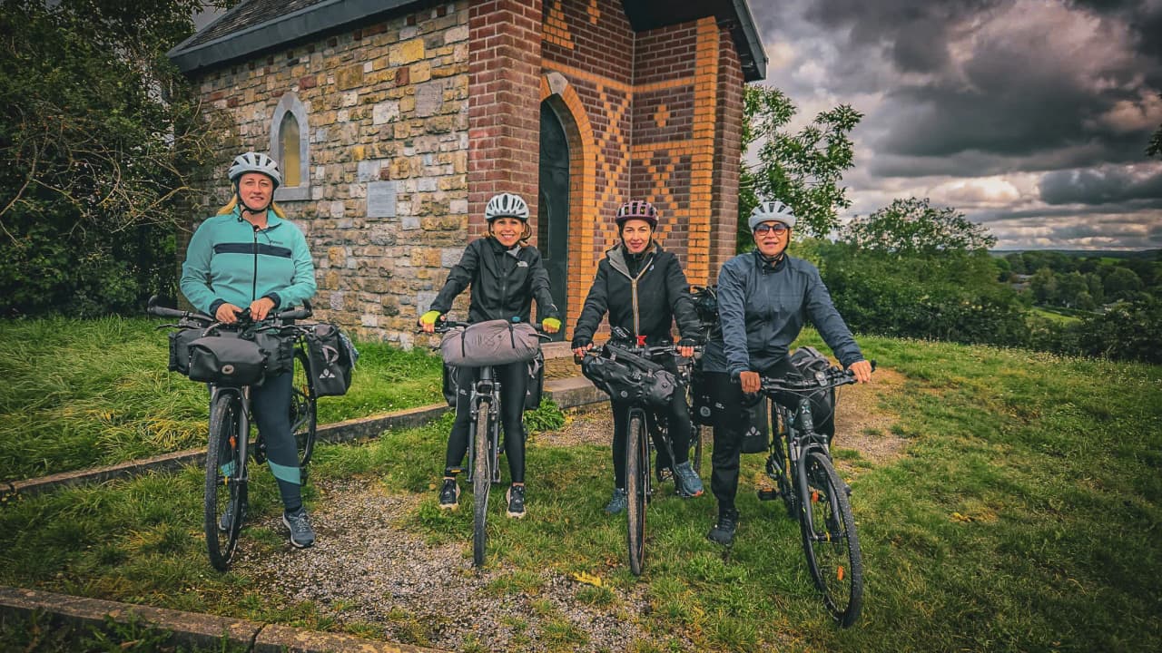 Vier uitgeruste fietsers, klaar om de Hoge Venen te verkennen, voor een charmante kapel.