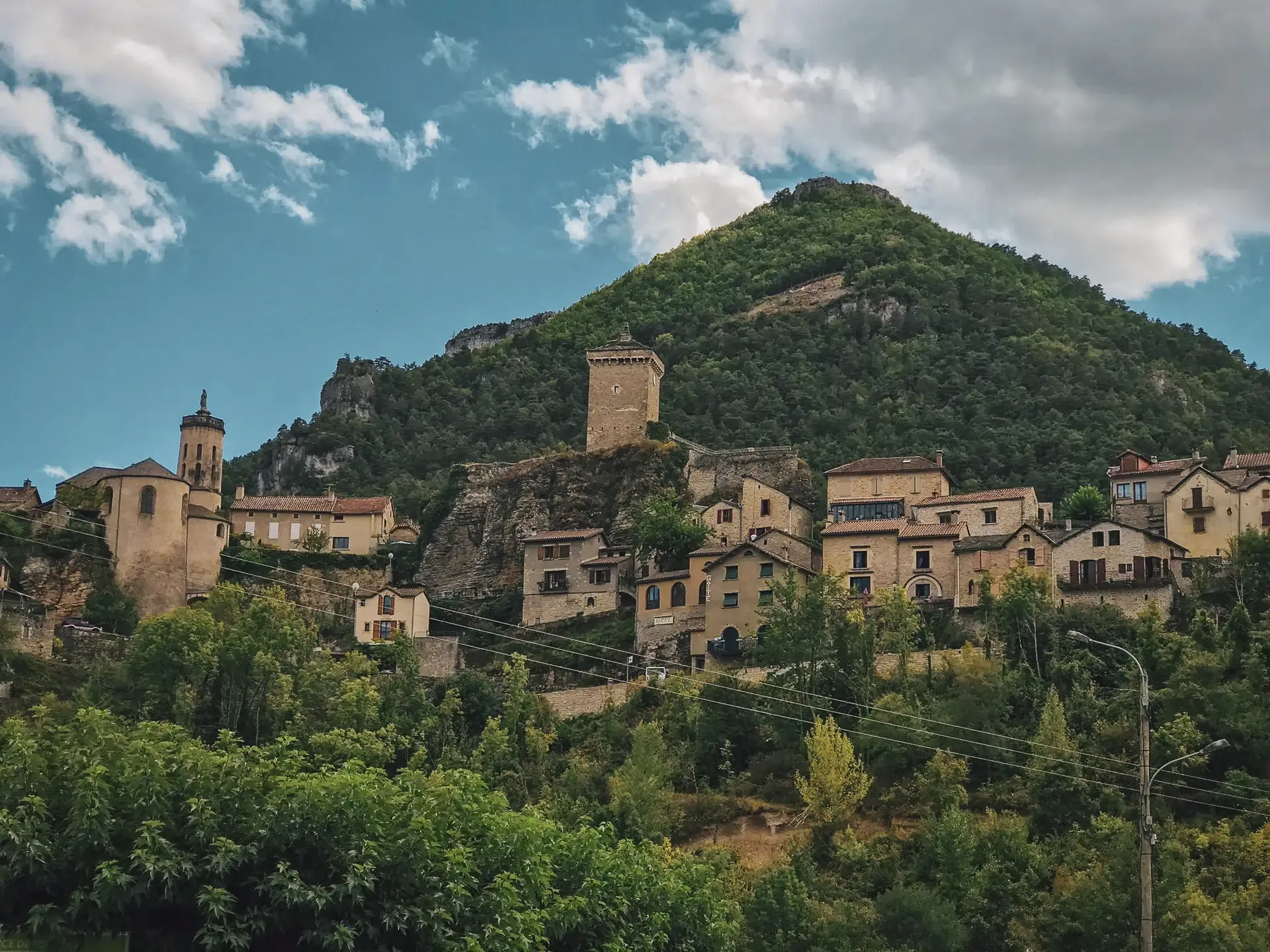 Village pittoresque perché sur une colline, entouré de verdure, sous un ciel nuageux.