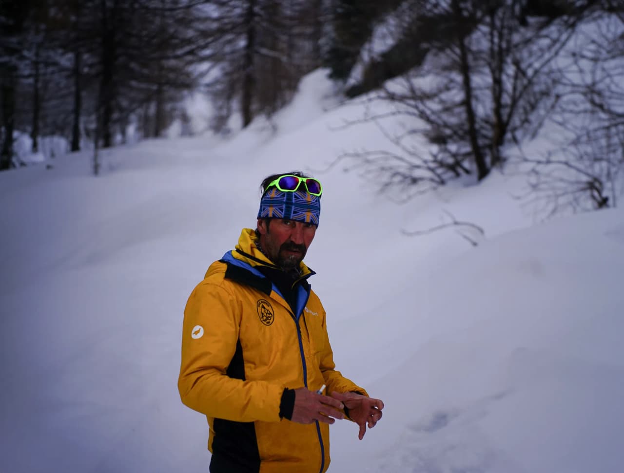 Un homme en veste jaune dans un paysage alpin enneigé, prêt pour l'aventure en montagne.