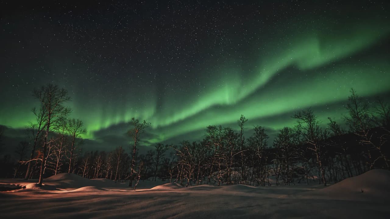 Het noorderlicht verlicht een sterrenhemel boven een besneeuwd landschap in Tromsø.