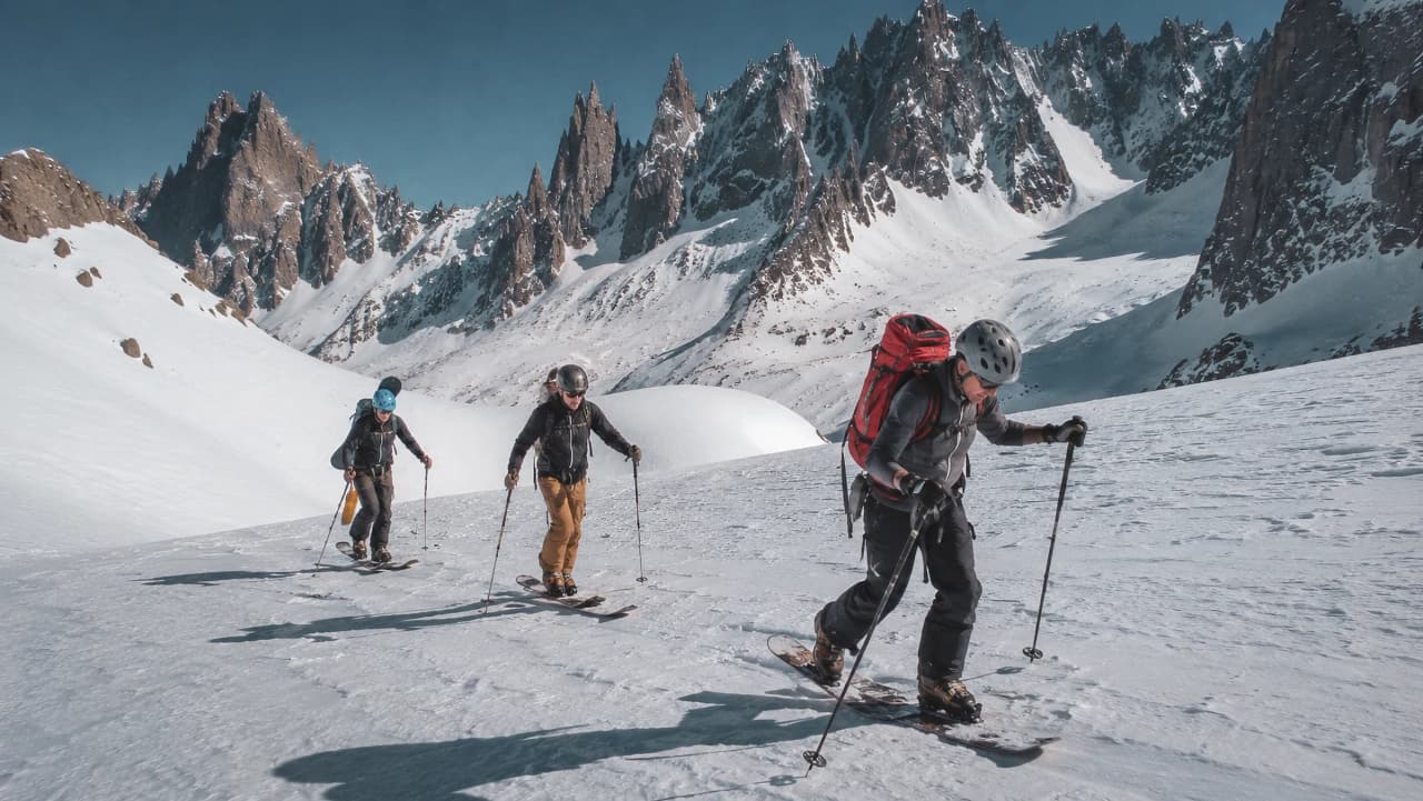 Groupe de snowboarders en randonnée sur glacier, face aux majestueuses montagnes du Mont-Blanc.