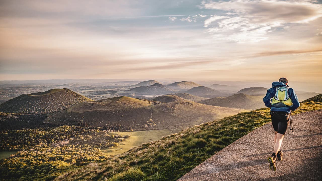 Runner on a volcanic trail in the Auvergne, with mountains on the horizon at sunset.