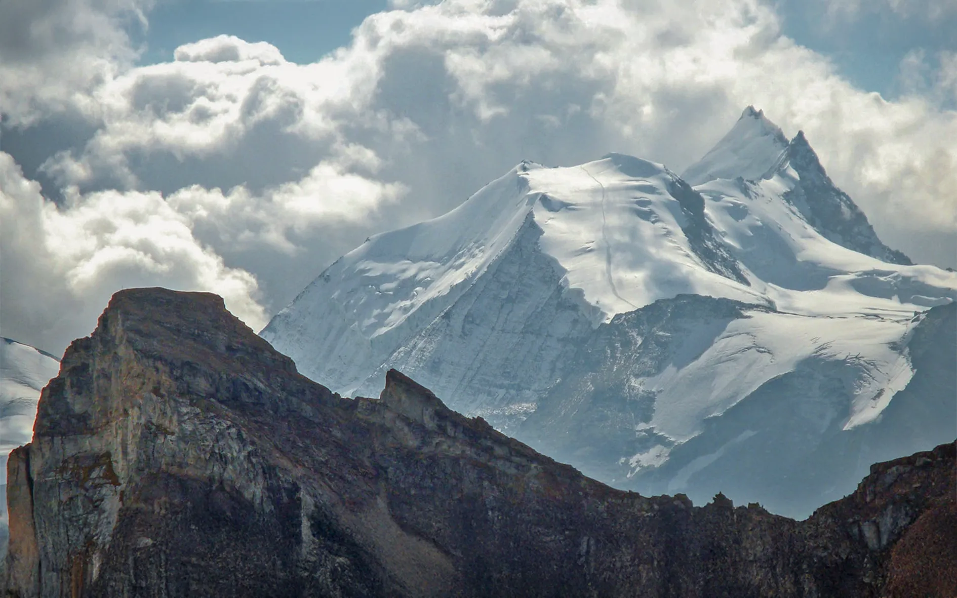 A snow-covered mountain landscape with high peaks, steep slopes and glacial formations.