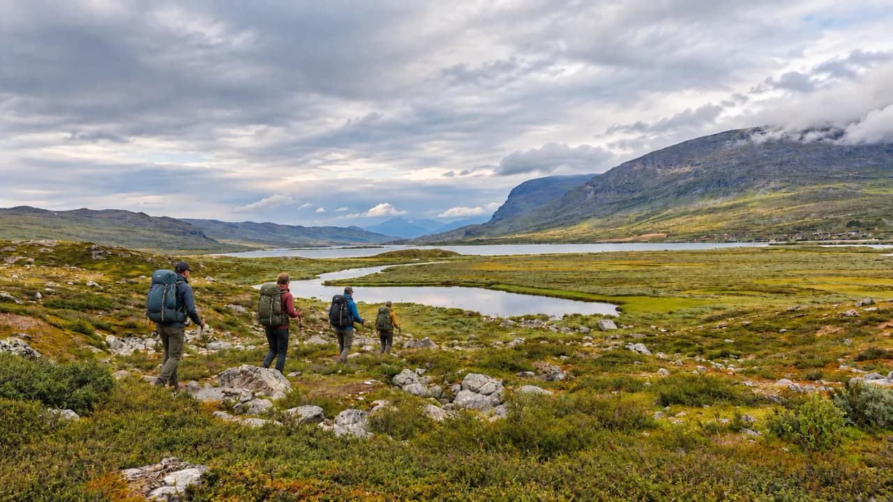 Randonneurs admirant les paysages sauvages de Laponie suédoise au bord d'un lac scintillant.