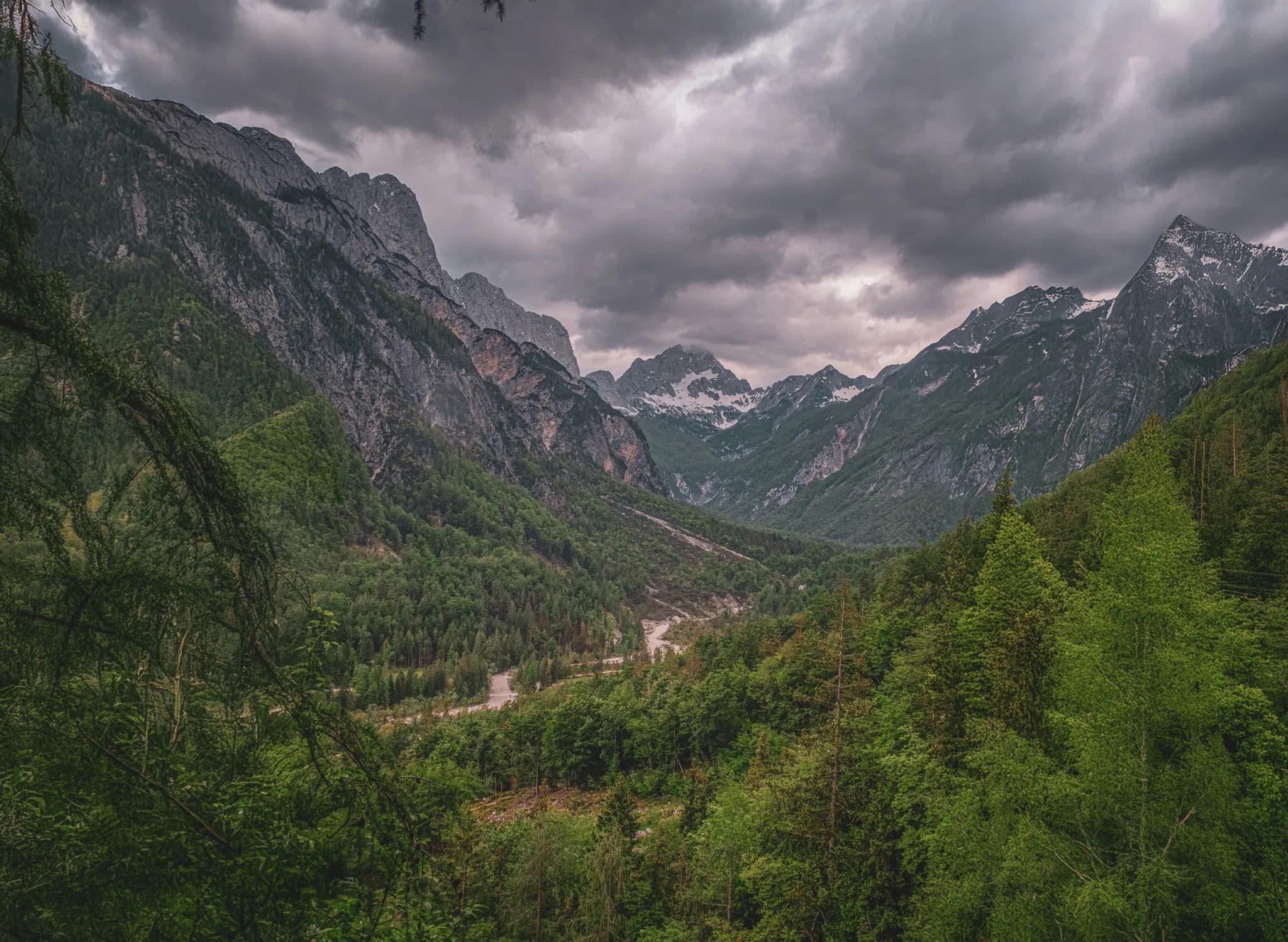 Vaste vallée alpine sous un ciel nuageux, entourée de majestueuses montagnes verdoyantes.