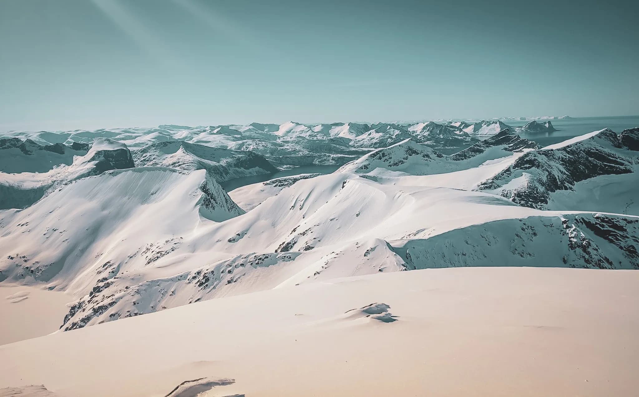Een spectaculair besneeuwd berglandschap, met majestueuze toppen in verschillende vormen. De bergkammen zijn golvend en de hellingen zijn bedekt met een dikke laag sneeuw die het licht van de zon weerkaatst.