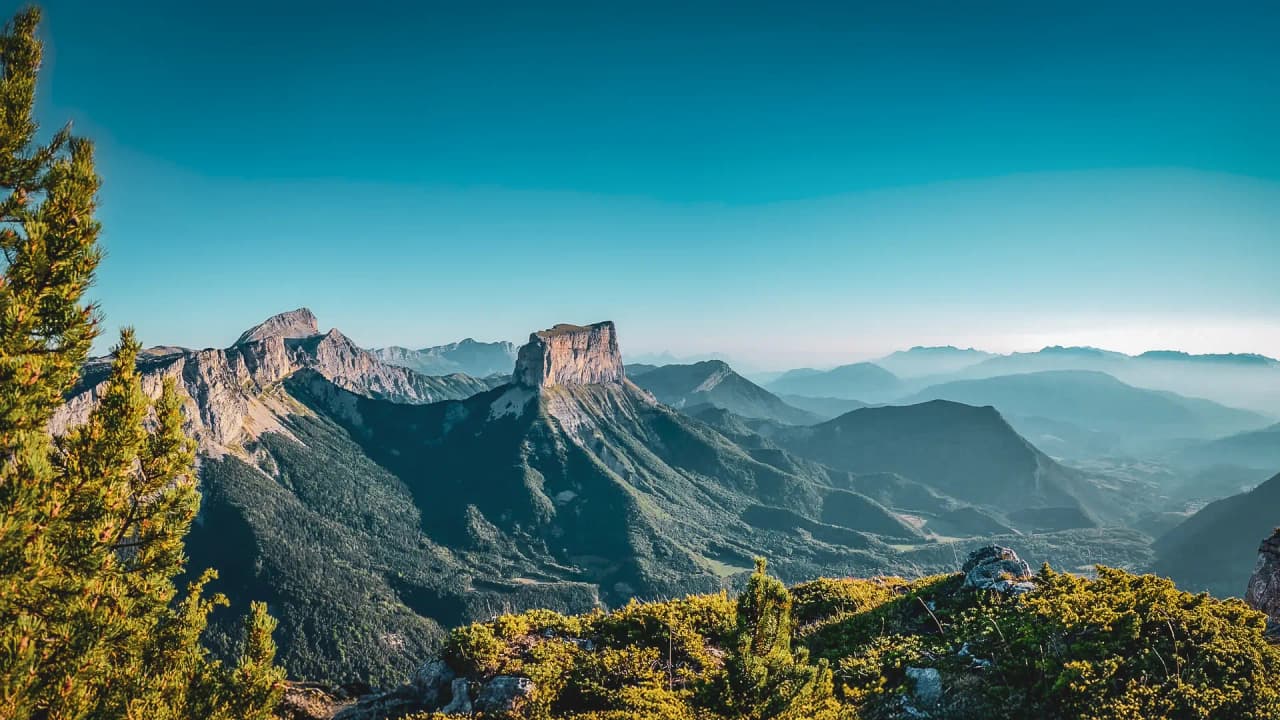 Vue panoramique des Hauts Plateaux du Vercors, parsemée de montagnes majestueuses et d'un ciel azuré.