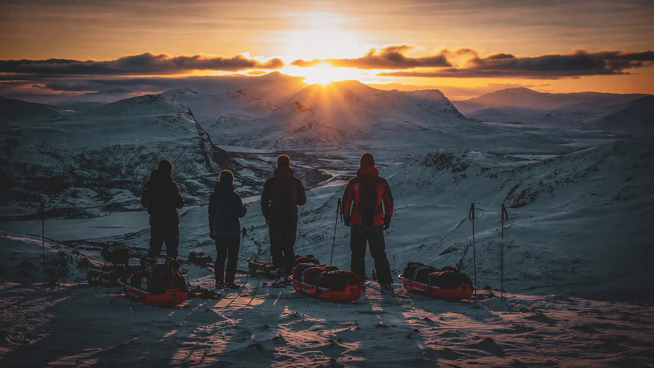 Vier avonturiers kijken naar de zonsopgang boven de besneeuwde bergen van Lapland.