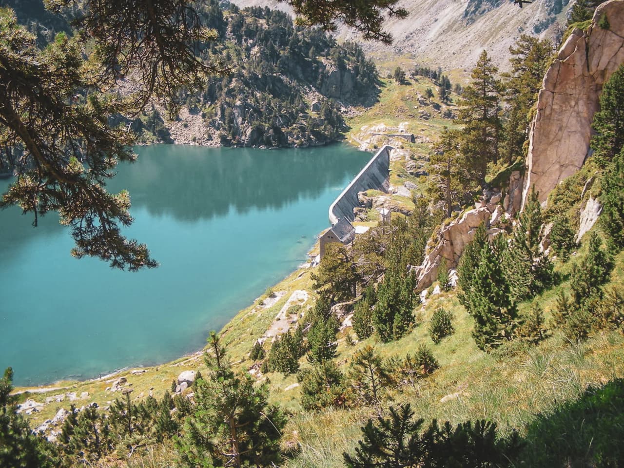 A turquoise lake fringed by rocks, with a lock and lush conifers in the background.