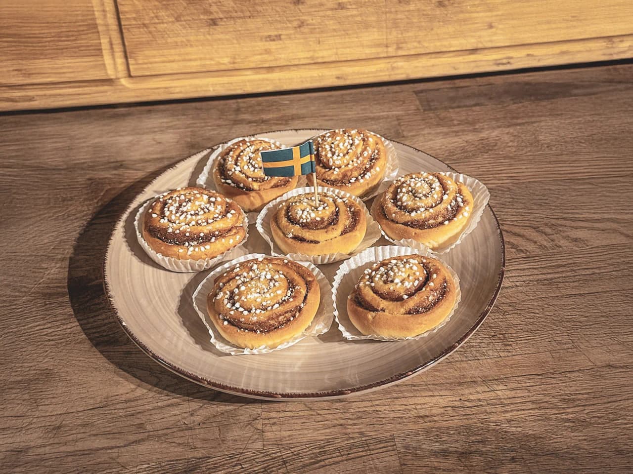 Sept délicieuses cinnamon rolls sur une assiette, décorées de sucre, évoquant la douceur de la Laponie.