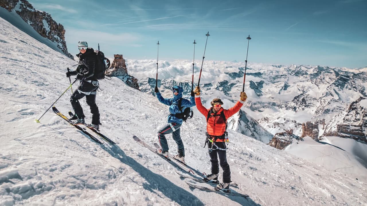 Three jubilant skiers on the snow-covered summit of Gran Paradiso, with breathtaking panoramic views.