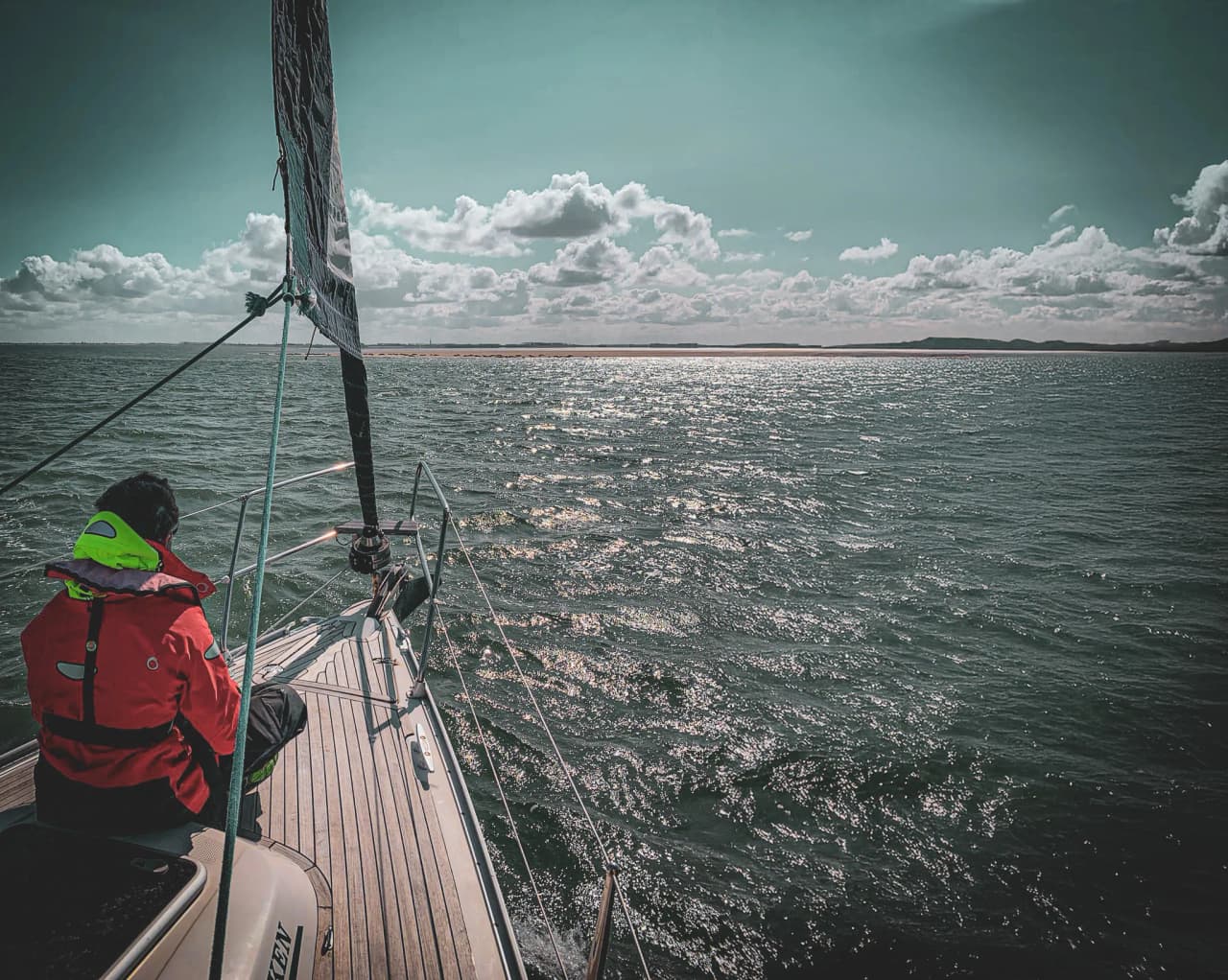 Een zeeman kijkt uit over de glinsterende horizon van een brede, bewolkte hemel.