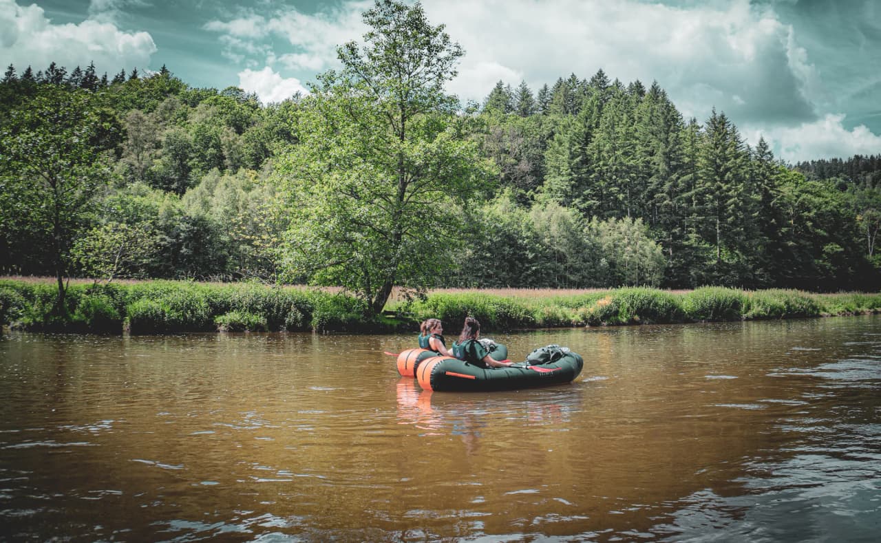 Twee avontuurlijke vrouwen peddelden rustig in een packraft op een rivier omringd door weelderig groen.