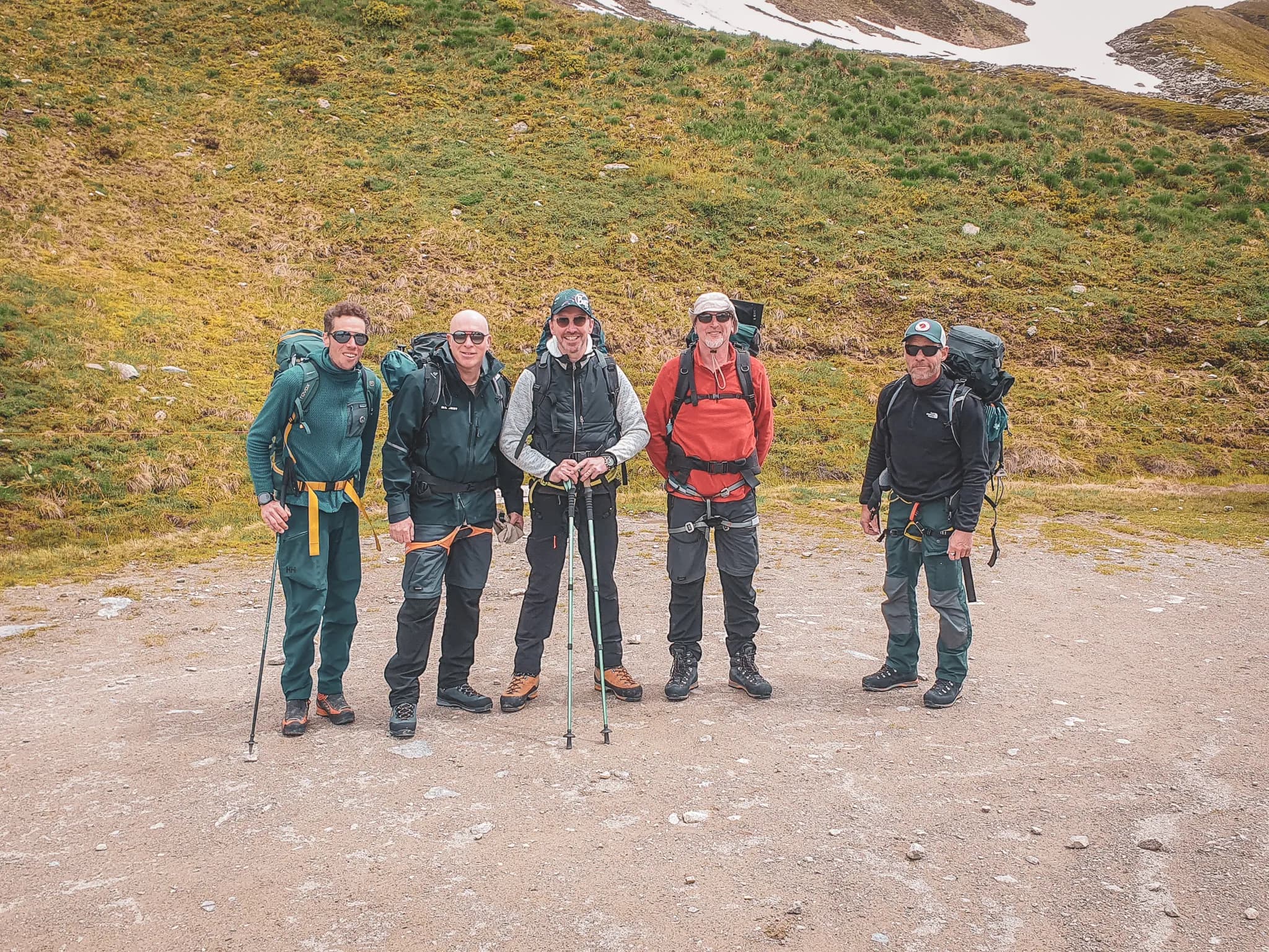 Five smiling hikers, equipped for a mountain adventure, surrounded by lush green landscapes.